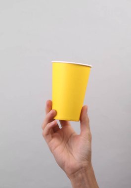 Gri arka planda tek kullanımlık sarı karton bardak tutan kadın.