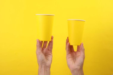 Sarı arka planda tek kullanımlık sarı karton bardakları tutan kadın.