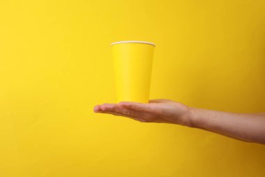 Sarı arka planda tek kullanımlık sarı karton bardak tutan kadın.