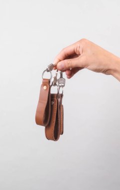 Gri arka planda kadın eli olan deri anahtarlıklar.