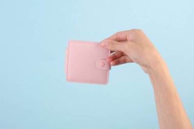Mavi arka planda pembe deri cüzdan tutan bir kadın.