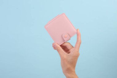 Mavi arka planda pembe deri cüzdan tutan bir kadın.