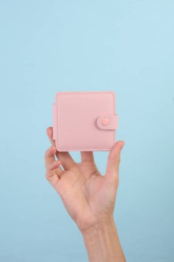 Female hand holding pink leather wallet on blue background