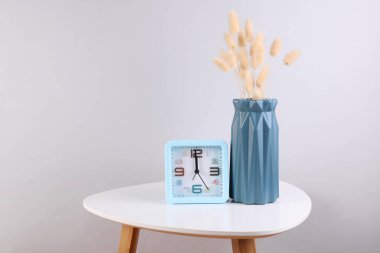 Kurumuş çiçekli vazo ve kahve masasında çalar saat.