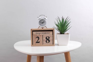 28 Eylül tarihli ahşap takvim düzenleyici ve dekoratif bitki, masa üzerinde çalar saat