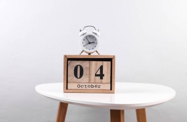 Tahta takvim düzenleyicisi, tarihi Ekim 04 ve masada çalar saat.