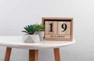 Ahşap takvim düzenleyicisi, tarih 19 Ekim ve masa üzerinde dekoratif bitkiler.
