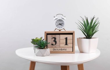 Tahta takvim düzenleyicisi. Tarihi 31 Ekim ve dekoratif bitkiler. Masada çalar saat.
