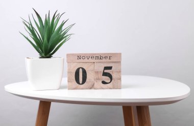 Wooden calendar organizer with date november 5 and decorative plant on table