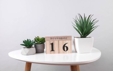 Wooden calendar organizer with date november 16 and decorative plants on table