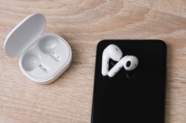 Şarj kutusu ve akıllı telefonu olan beyaz kablosuz kulaklıklar.