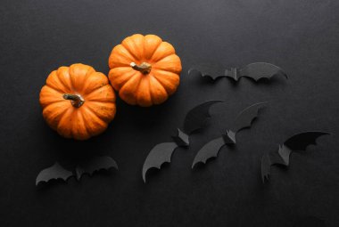 Paper cut black bats and pumpkins on black background. Halloween decor. Flat lay