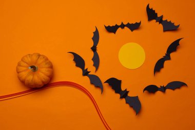 Handmade paper cut out halloween scene with bats and moon, pumpkin on orange background