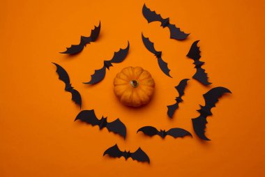 Kağıt turuncu arka planda siyah yarasalar ve balkabakları kesiyor. Cadılar Bayramı dekoru. Düz yatıyordu