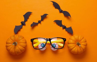 Gözlüklü gözler, yarasalar ve turuncu arka planda balkabakları. Minimalizm cadılar bayramı hala hayat. Düz yatıyordu