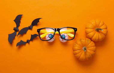 Gözlüklü gözler, yarasalar ve turuncu arka planda balkabakları. Minimalizm cadılar bayramı hala hayat. Düz yatıyordu
