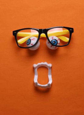 Gözlüklü ve turuncu arka planda vampir çeneli gözler. Canavar suratlı. Cadılar Bayramı hayat dolu