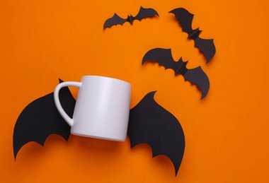 Tasarımınız için beyaz seramik kupa modeli ve turuncu arka planda Cadılar Bayramı dekoratif yarasalar