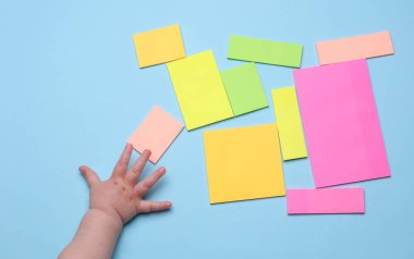 Çocuklar ellerinde çok renkli çıkartmalar olan boş kağıt tutuyorlar. Mavi arkaplanda yapışkan not koleksiyonu