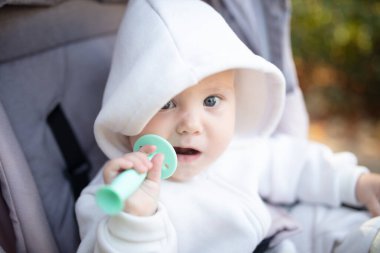 Kapüşonlu, dişlek, dışarıda bebek arabasında oturan tatlı bir bebek.