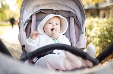 Kapüşonlu, dişlek, dışarıda bebek arabasında oturan tatlı bir bebek.