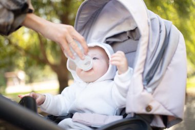 Kapüşonlu bir bebek şişeden su içiyor ve bebek arabasında oturuyor.
