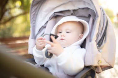 Kapüşonlu küçük şirin bir bebek, bebek arabasının içinde oturmuş ip çiğniyor.