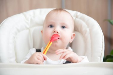 Sevimli bebek kaşıkla yemek masasında oturuyor.