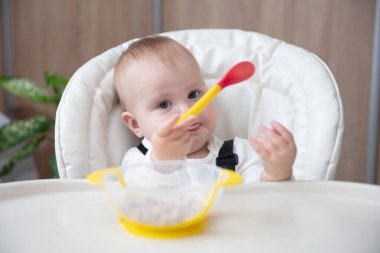 Beslenme masasında otururken kaşıkla yemek yiyen tatlı bir bebek.