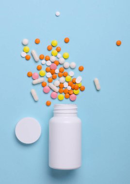 Mavi arka planda hapları olan beyaz plastik şişe. Tıp konsepti. Tasarım için model