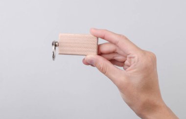 Gri arka planda tahta anahtarlık tutan kadın.