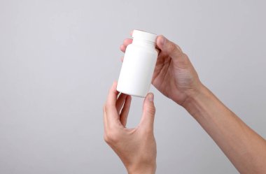 Beyaz plastik hap şişesi. Gri arka planda kadın ellerinde. Tasarım için model, tıp konsepti