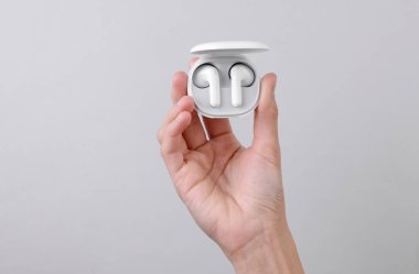 Gri arka planda şarj durumunda kablosuz kulaklık tutan bir kadın.