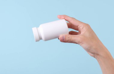 Mavi arka planda beyaz plastik hap şişesi var. Tasarım için model, tıp konsepti