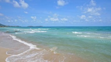 Deniz dalgaları, kumlu sahil ve mavi gökyüzü olan pitoresk bir marina.