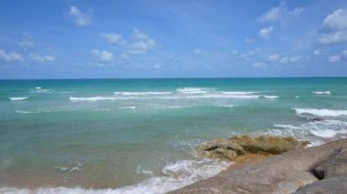 Deniz dalgaları, kumlu sahil ve mavi gökyüzü olan pitoresk bir marina.