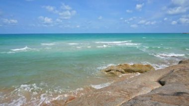 Deniz dalgaları, kumlu sahil ve mavi gökyüzü olan pitoresk bir marina.