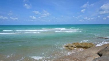 Deniz dalgaları, kumlu sahil ve mavi gökyüzü olan pitoresk bir marina.