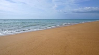 Deniz dalgaları, kumlu sahil ve mavi gökyüzü olan pitoresk bir marina.