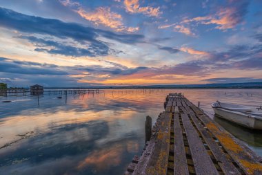 Ahşap bir iskelede teknesi olan bir göl kıyısında inanılmaz bir gün batımı.