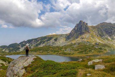 Bir kadın tepeden kayanın üzerinde güzel bir manzaranın tadını çıkarır. Dağlarda seyahat et..