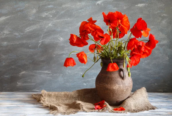 Stillleben im rustikalen Stil: ein alter Topf und ein Strauß roter Mohnblumen auf einem Holztisch — Stockfoto