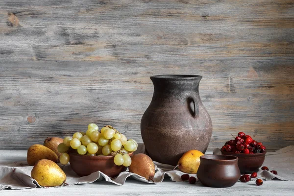 Натюрморт в сільському стилі: набір глиняних посуду, винограду і груш на дерев'яному столі. Натуральне світло з вікон . — стокове фото