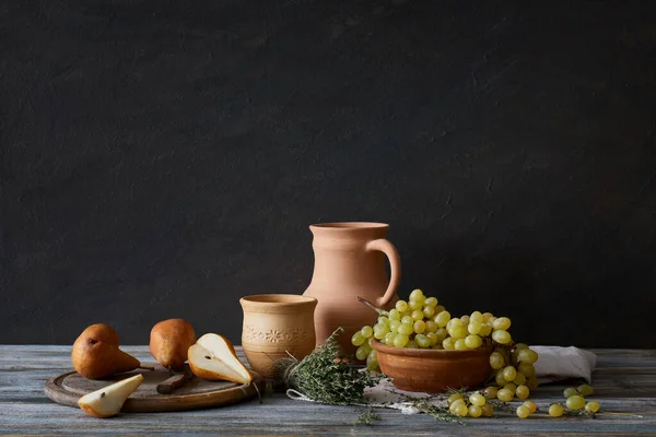 Still life in a rustic style: a set of clay dishes, grapes and pears on a wooden table. Natural light from the windows.
