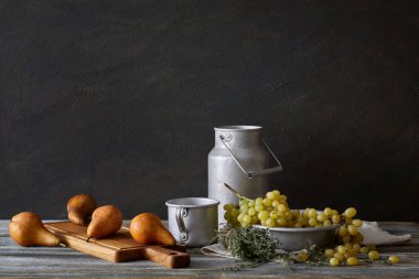 Köy tarzında sakin bir hayat: ahşap bir masada bir dizi alüminyum tabak, üzüm ve armut. Pencerelerden gelen doğal ışık.
