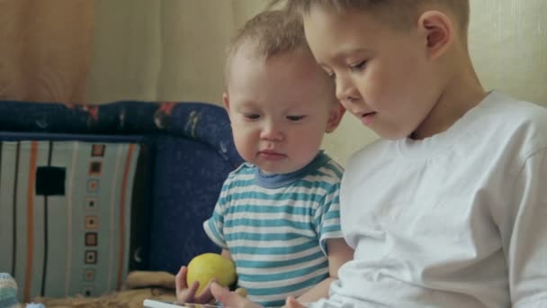 Zwei junge weiße Kinder spielen mit einem Tablet. — Stockvideo