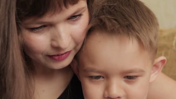 Allegro bambino e sua madre seduti sul divano con un tablet digitale — Video Stock