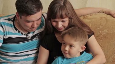 Neşeli küçük çocuk ve dijital tablet kullanırken koltukta oturan ailesi