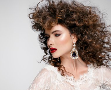 Güzel genç kadın uzun kahverengi saçlı, kırmızı dudaklar, mücevher gelinlikle oldukça pozlar stüdyoda modeli.