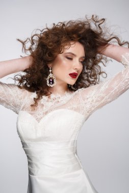 Güzel genç kadın uzun kahverengi saçlı, kırmızı dudaklar, mücevher gelinlikle oldukça pozlar stüdyoda modeli.